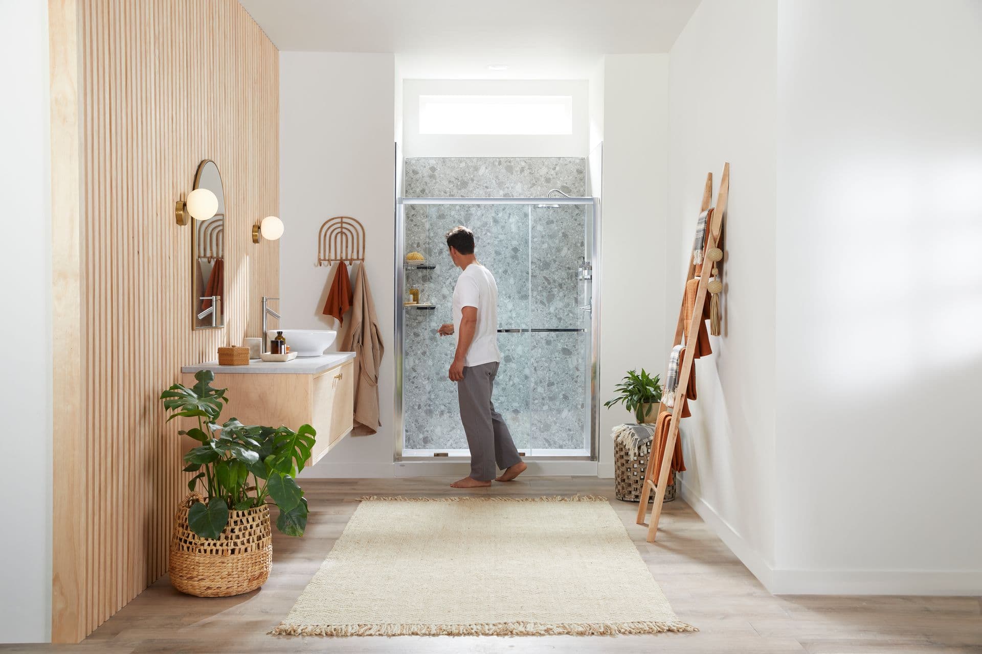 A photo of a shower with a Terrazzo Latte wall and Dual ByPass sliding Doors. A model is opening the shower doors, facing away from camera.