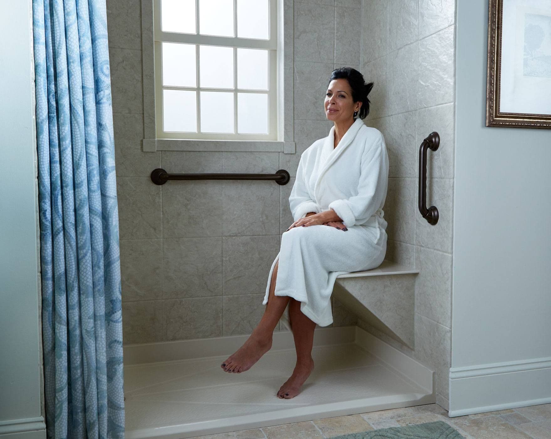 A model in a white bathroom sitting on a Stone Bench in a Barrier Free Tahiti shower