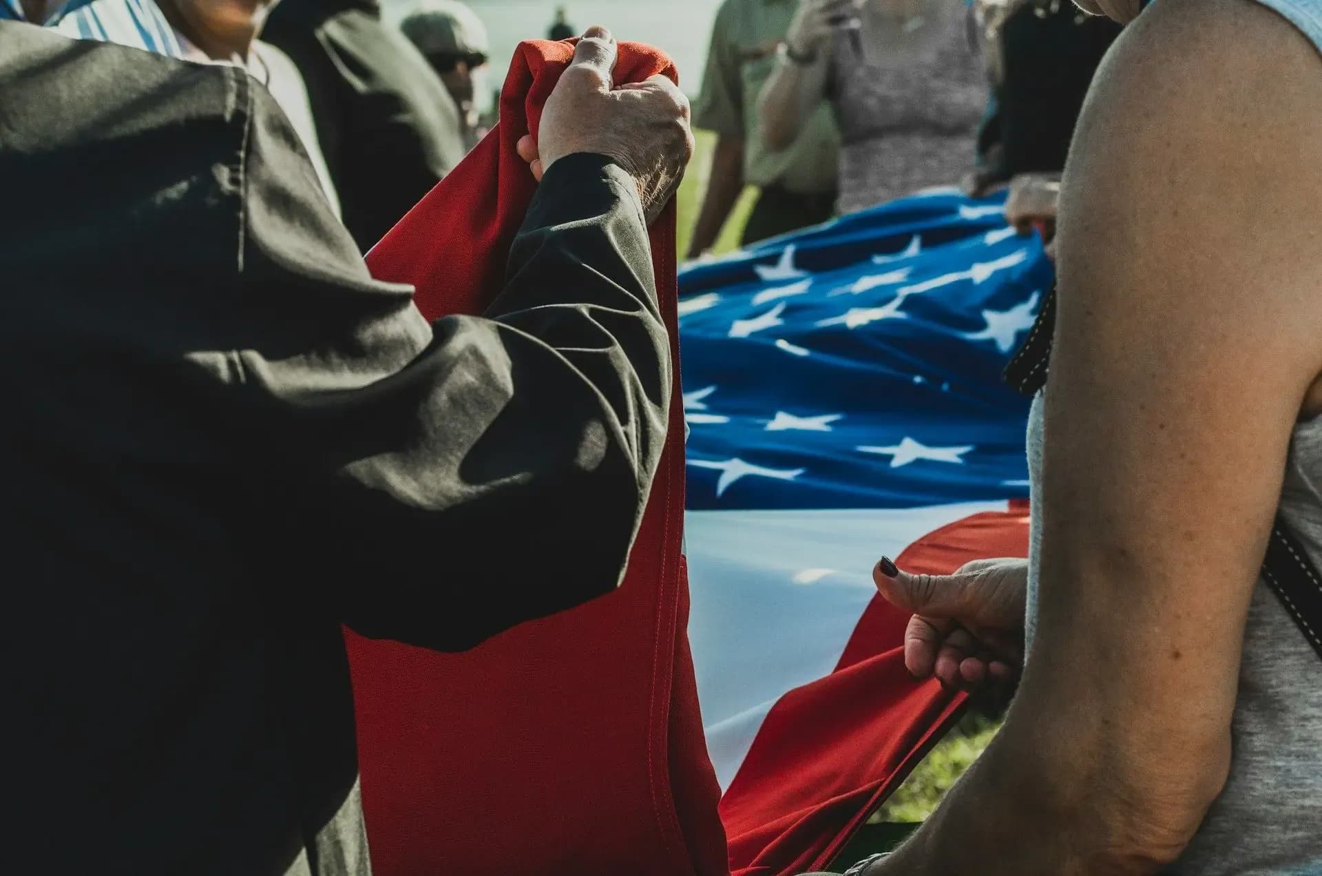 A photo of multiple people folding an American flag, as in a military ceremony.